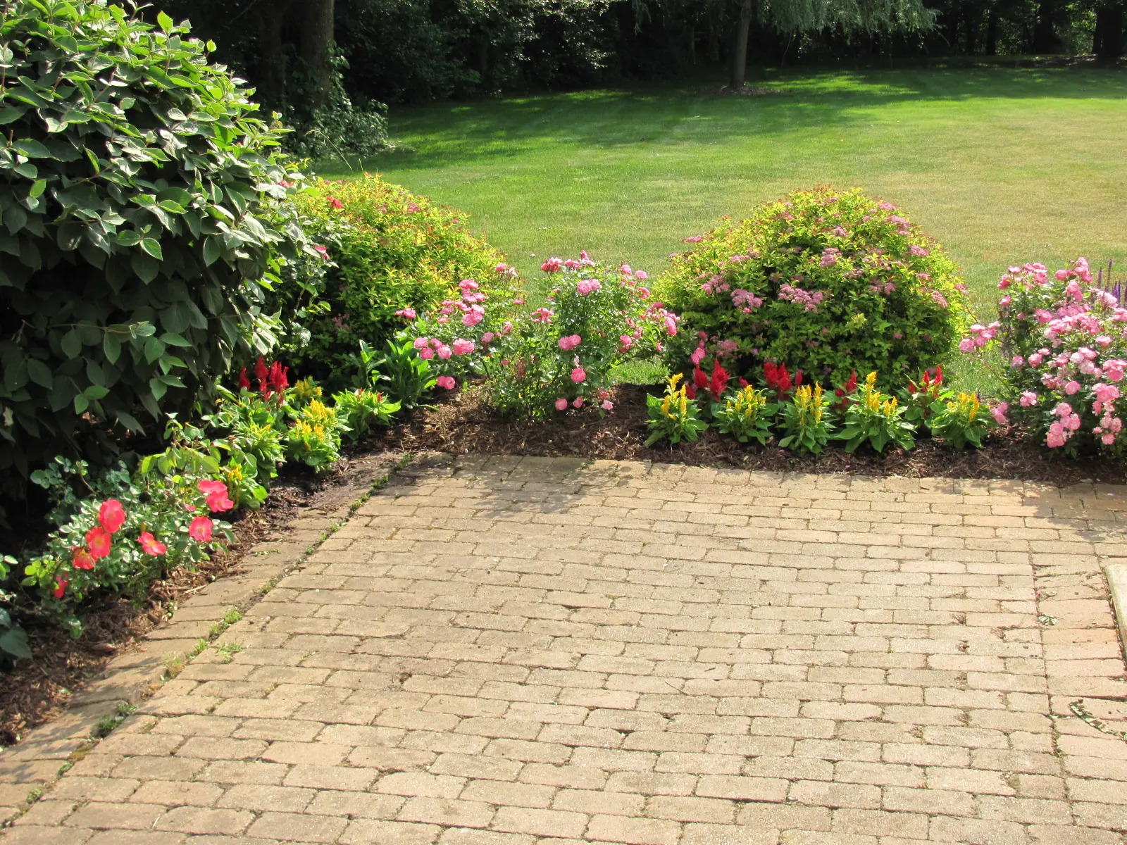 A brick patio with flowers and bushes in the background.